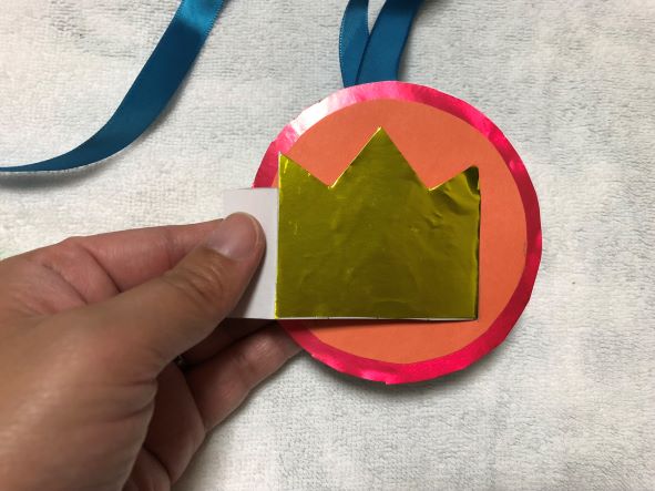 王冠をメダルに差し込み、テープでとめる